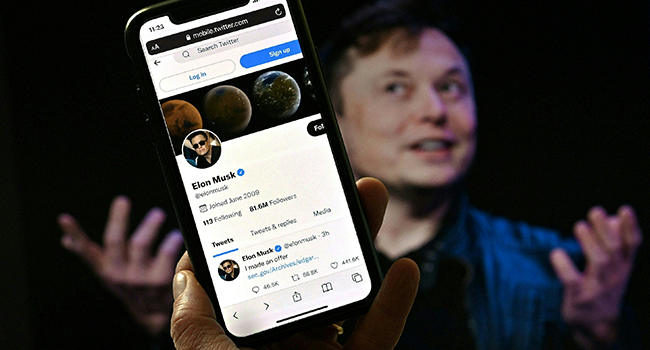 In this photo illustration, a phone screen displays the Twitter account of Elon Musk with a photo of him shown in the background, on April 14, 2022, in Washington, DC. Olivier DOULIERY / AFP